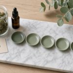 Indications du cannabis médical en France : bocal de fleurs, flacon ambré et cinq coupelles vert sauge sur marbre blanc avec carte à croix verte et eucalyptus