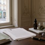 Bureau en bois d’un bureau parlementaire avec liasses de projet de loi et d’amendements, flacon compte-gouttes ambré, petit bocal de fleurs séchées, plante verte et croix médicale verte
